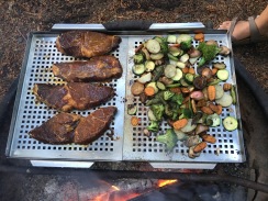 Photo of steak and veggies grilling over a campfire